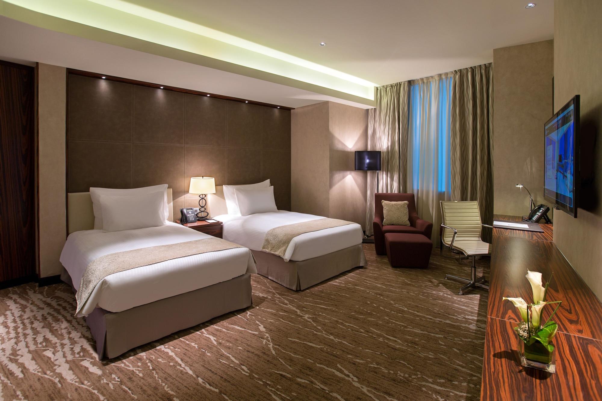Millennium Plaza Doha Hotel Exterior photo The photo shows a modern hotel room featuring two twin beds with white bedding positioned against a stylish wall. The room has a neutral color scheme with elegant decor, including a bedside lamp and a small table. There is a plush armchair in one cor
